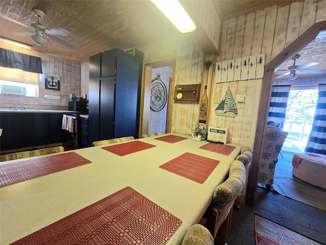 dining room featuring ceiling fan, wood walls, and sink