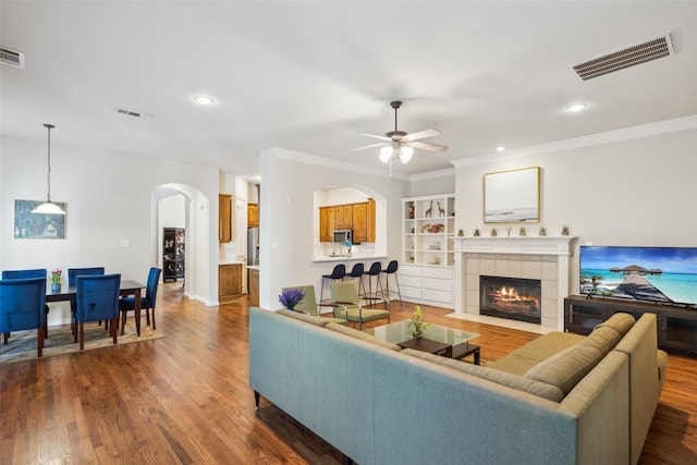 living room with dark wood-type flooring, ceiling fan, ornamental molding, and a fireplace