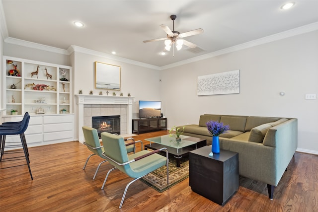 living room featuring ceiling fan, hardwood / wood-style flooring, ornamental molding, and a tile fireplace