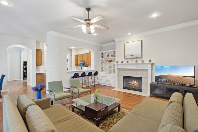 living room featuring a tile fireplace, crown molding, light hardwood / wood-style floors, and ceiling fan