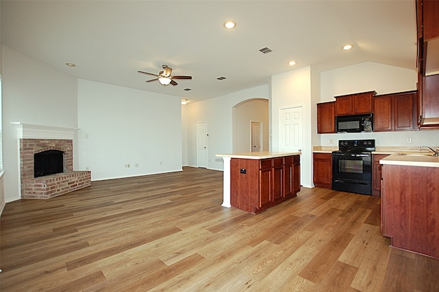 kitchen with light hardwood / wood-style floors, lofted ceiling, black appliances, and a brick fireplace