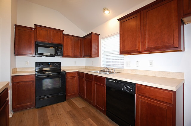 kitchen with sink, black appliances, vaulted ceiling, and hardwood / wood-style floors