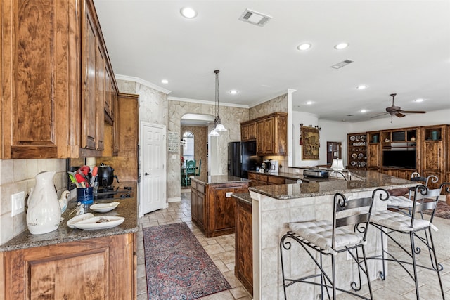 kitchen with kitchen peninsula, ceiling fan, black fridge with ice dispenser, dark stone countertops, and a center island