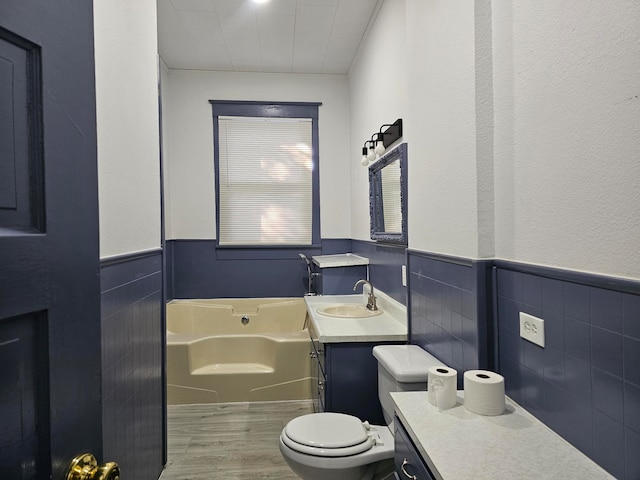 bathroom featuring hardwood / wood-style floors, tile walls, toilet, a bath, and vanity