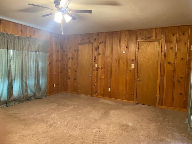 carpeted empty room with wooden walls and ceiling fan