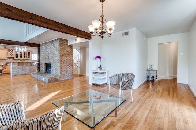 living room with beam ceiling, light wood-type flooring, a brick fireplace, a notable chandelier, and brick wall