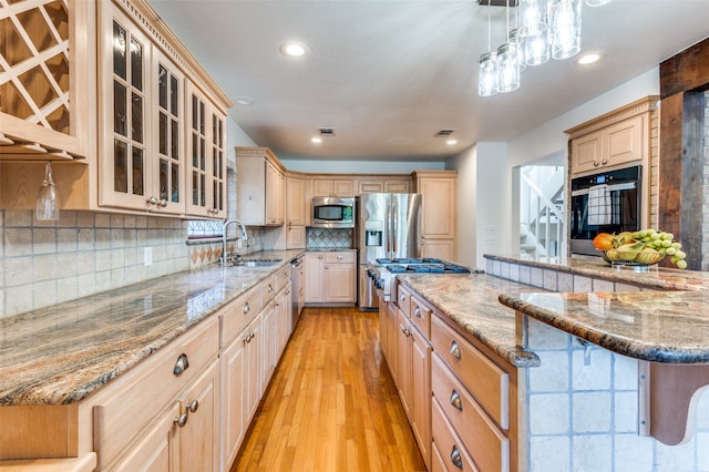 kitchen with hanging light fixtures, appliances with stainless steel finishes, a breakfast bar, light wood-type flooring, and sink