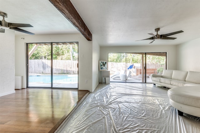 living room with ceiling fan, hardwood / wood-style flooring, beamed ceiling, and a textured ceiling