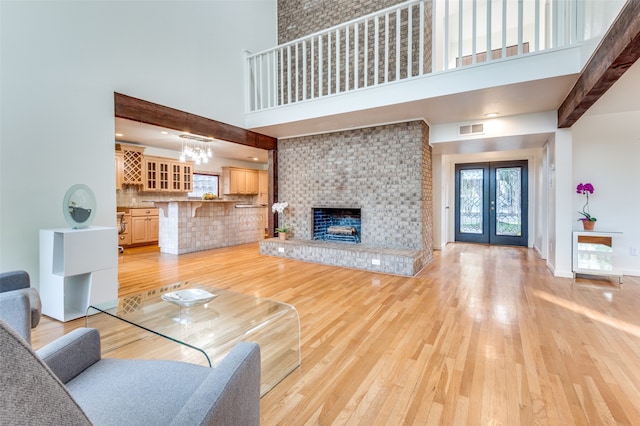 living room featuring french doors, light hardwood / wood-style flooring, a high ceiling, and a brick fireplace