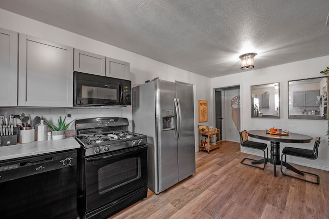 kitchen featuring black appliances, light wood-type flooring, backsplash, a textured ceiling, and gray cabinets