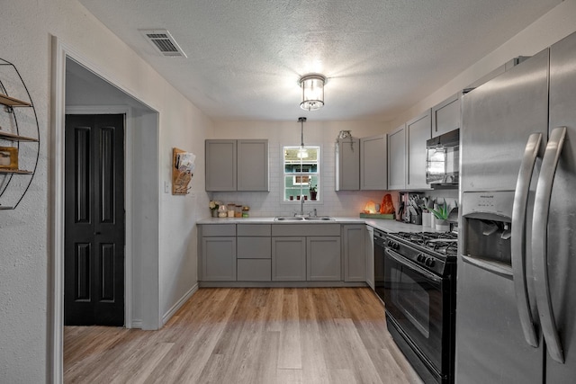 kitchen with a textured ceiling, light wood-type flooring, black appliances, gray cabinetry, and sink