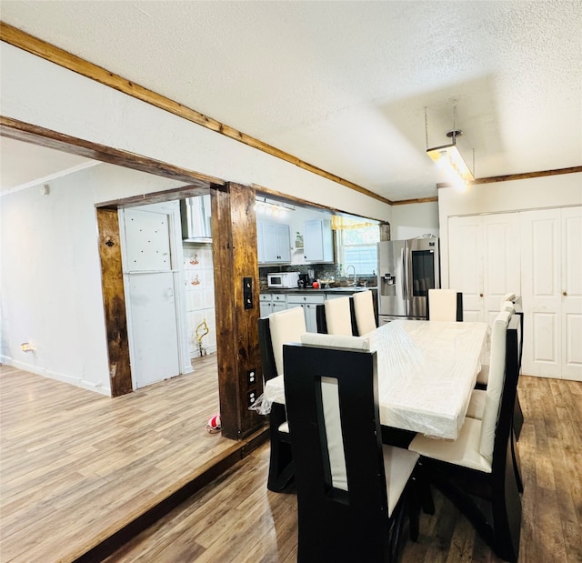 dining room with ornamental molding, sink, light hardwood / wood-style flooring, and a textured ceiling