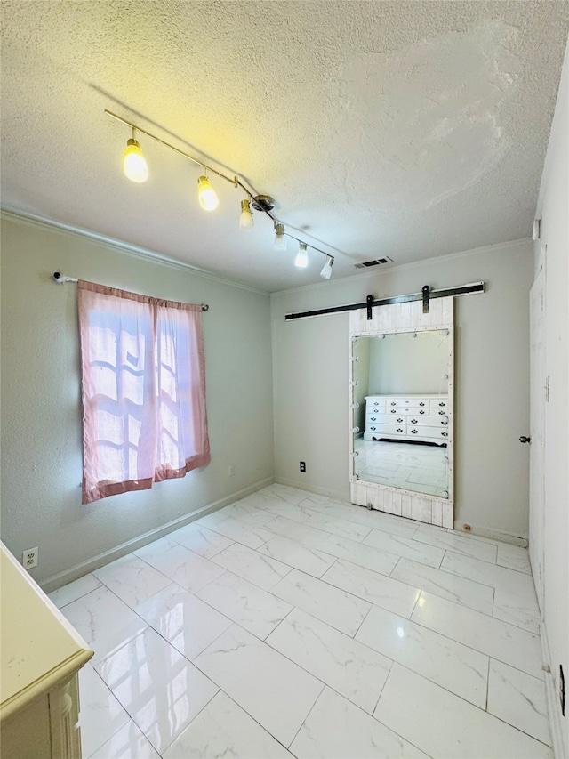 unfurnished room with ornamental molding, a barn door, a textured ceiling, and rail lighting