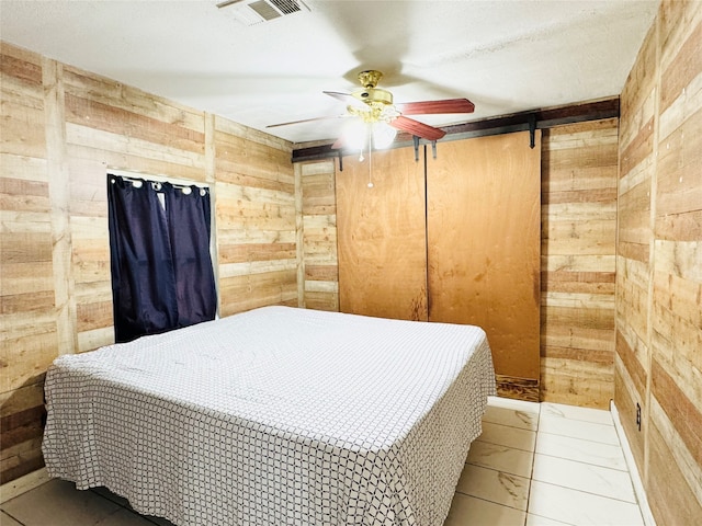 tiled bedroom with a barn door, wooden walls, and ceiling fan