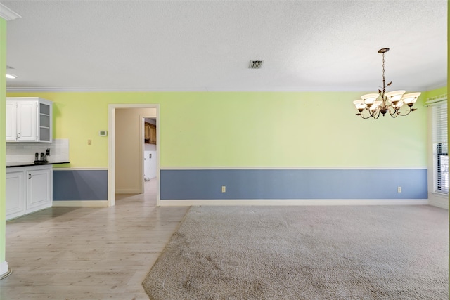 empty room with a notable chandelier, a textured ceiling, ornamental molding, and light hardwood / wood-style flooring