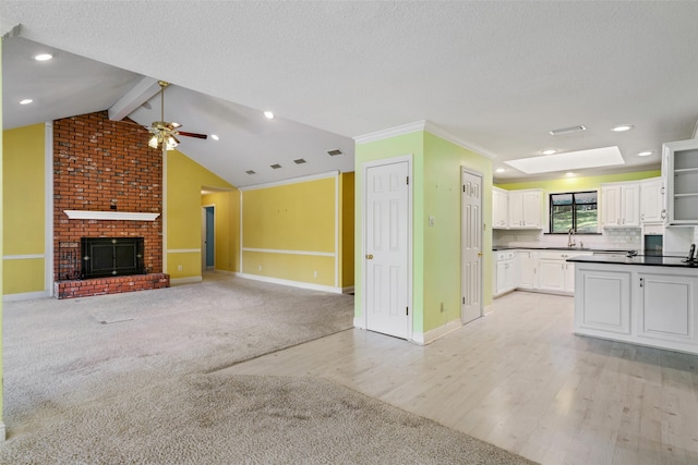 unfurnished living room with a textured ceiling, a brick fireplace, ceiling fan, vaulted ceiling with skylight, and light hardwood / wood-style flooring