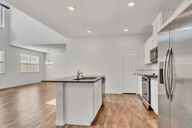 kitchen featuring an island with sink, stainless steel appliances, dark stone counters, sink, and white cabinets