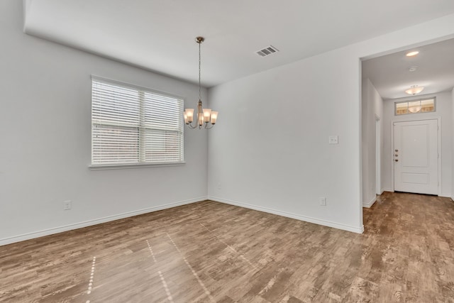 unfurnished room featuring an inviting chandelier and hardwood / wood-style flooring