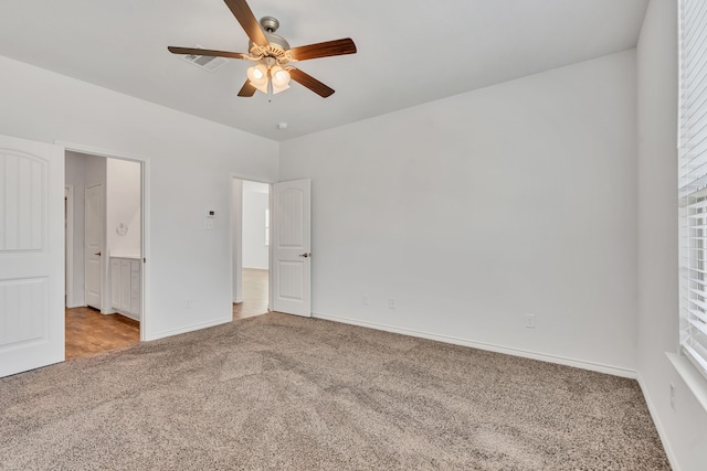 unfurnished bedroom featuring ceiling fan, multiple windows, light colored carpet, and ensuite bathroom