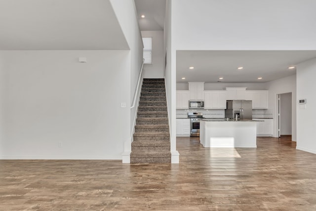 kitchen with tasteful backsplash, a center island with sink, white cabinetry, hardwood / wood-style flooring, and stainless steel appliances