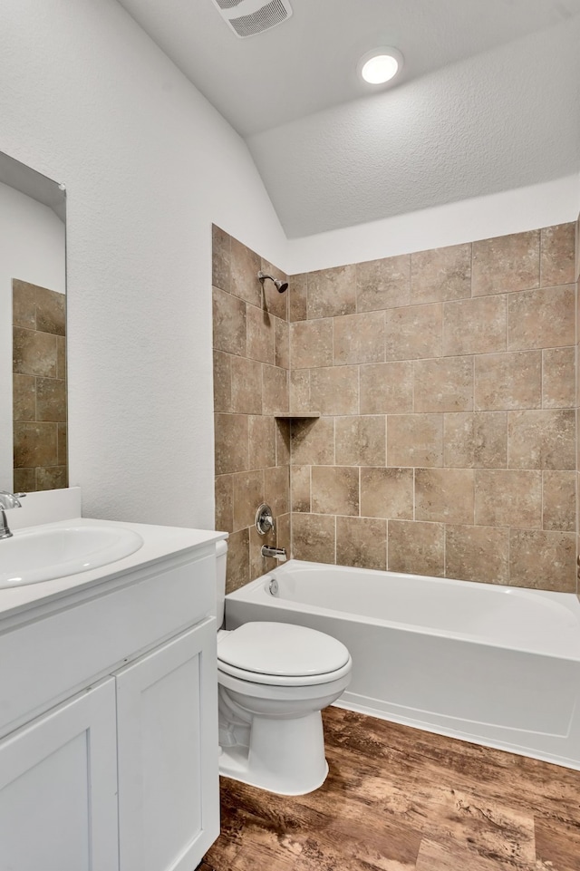 full bathroom with wood-type flooring, toilet, vaulted ceiling, tiled shower / bath, and vanity