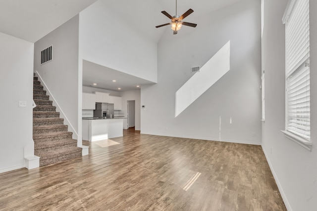 unfurnished living room with hardwood / wood-style floors, high vaulted ceiling, and ceiling fan