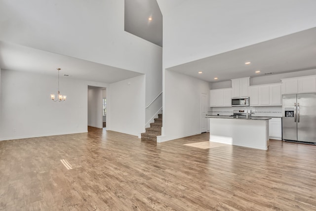 kitchen with white cabinets, a center island with sink, light hardwood / wood-style flooring, a high ceiling, and stainless steel appliances