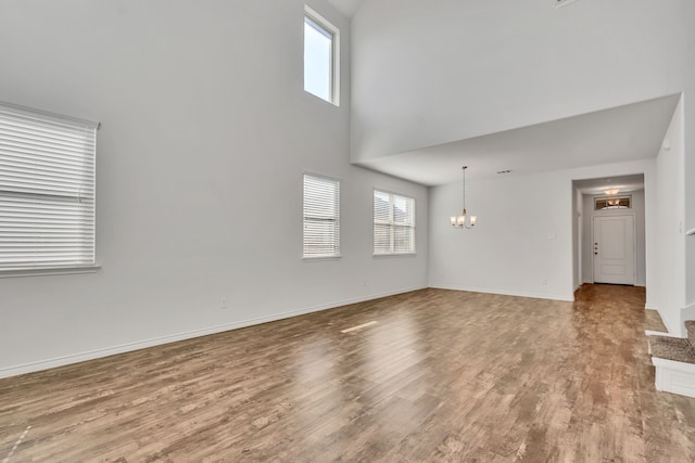 unfurnished living room with a notable chandelier, a towering ceiling, and light hardwood / wood-style flooring