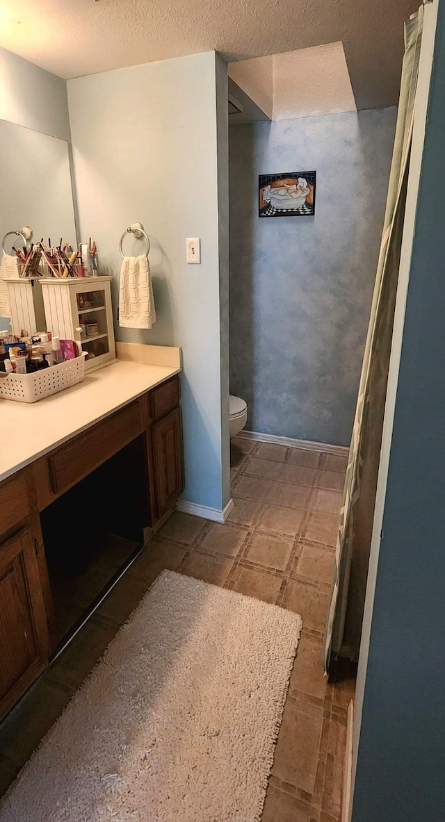 bathroom with toilet, baseboards, a textured ceiling, and vanity