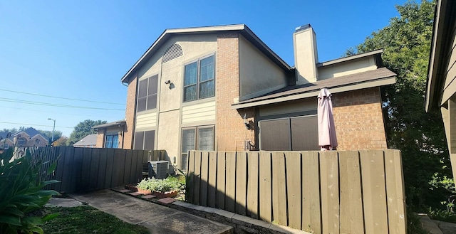 view of home's exterior featuring cooling unit, brick siding, fence, stucco siding, and a chimney