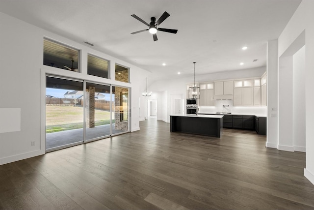 unfurnished living room with ceiling fan with notable chandelier and dark wood-type flooring