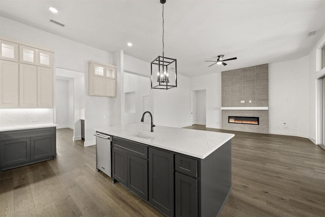 kitchen featuring ceiling fan with notable chandelier, white cabinets, hanging light fixtures, a tile fireplace, and a center island with sink