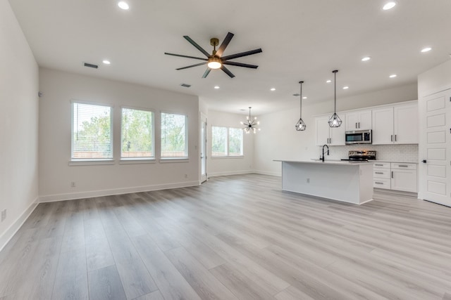 kitchen with stainless steel appliances, light hardwood / wood-style flooring, white cabinets, hanging light fixtures, and an island with sink