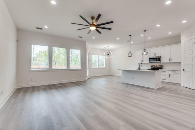 kitchen featuring hanging light fixtures, backsplash, stainless steel appliances, white cabinets, and a center island with sink