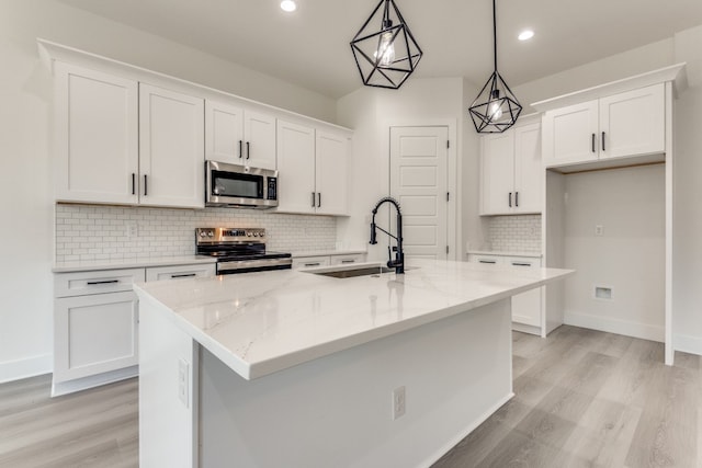 kitchen with a center island with sink, white cabinets, sink, appliances with stainless steel finishes, and decorative light fixtures