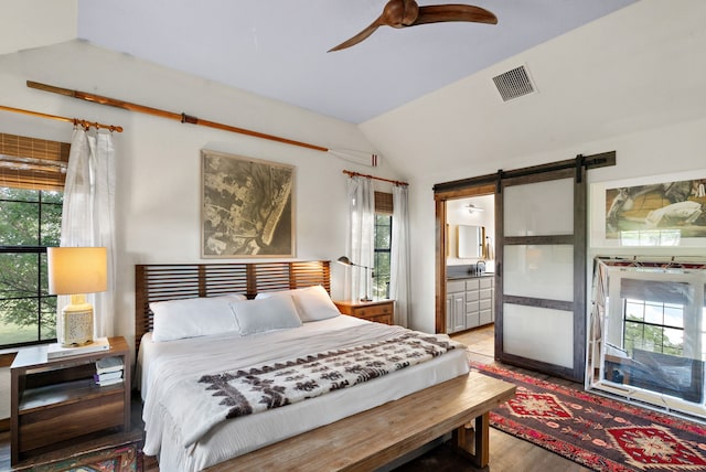 bedroom featuring connected bathroom, lofted ceiling, wood-type flooring, a barn door, and ceiling fan