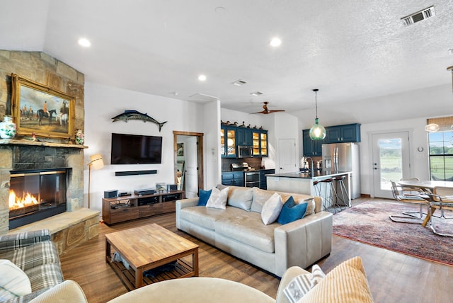 living room with a stone fireplace, a textured ceiling, hardwood / wood-style floors, ceiling fan, and lofted ceiling