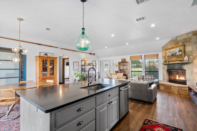 kitchen featuring sink, a stone fireplace, lofted ceiling, dark wood-type flooring, and a kitchen island with sink