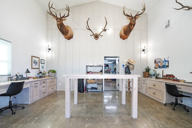 office with a towering ceiling, built in desk, and concrete flooring