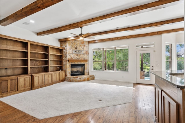 living room featuring ceiling fan, beam ceiling, hardwood / wood-style flooring, and a stone fireplace