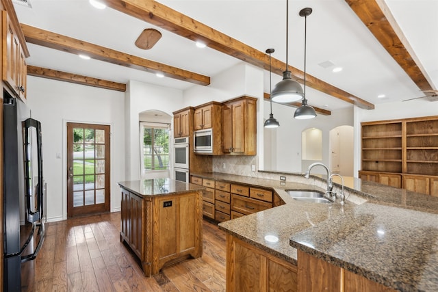 kitchen with hanging light fixtures, dark stone countertops, stainless steel appliances, dark wood-type flooring, and sink