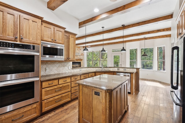 kitchen with a healthy amount of sunlight, stainless steel appliances, hanging light fixtures, and a kitchen island