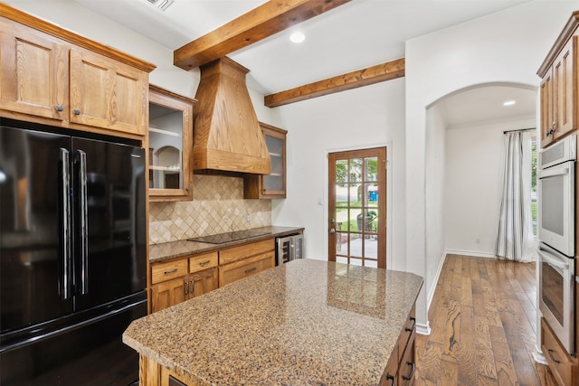 kitchen featuring black appliances, a kitchen island, beamed ceiling, light stone counters, and dark hardwood / wood-style floors