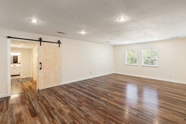 empty room with dark wood-type flooring, a barn door, and a textured ceiling