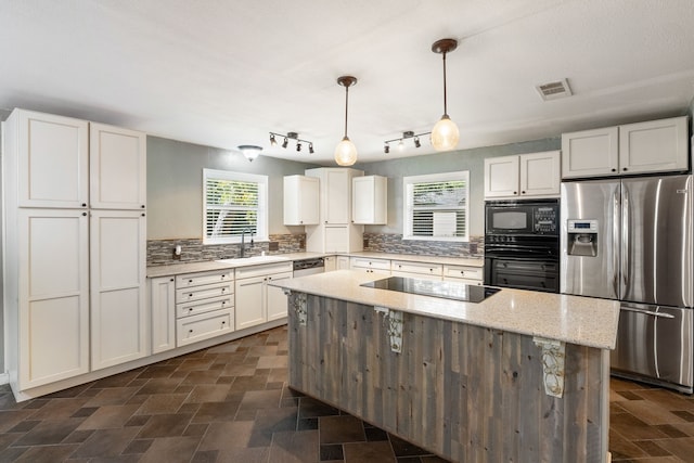 kitchen featuring a kitchen island, sink, black appliances, light stone countertops, and decorative light fixtures