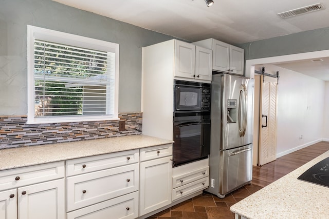 kitchen featuring light stone countertops, black appliances, a barn door, and white cabinets