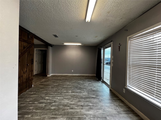 unfurnished room featuring a textured ceiling, dark hardwood / wood-style flooring, and a barn door