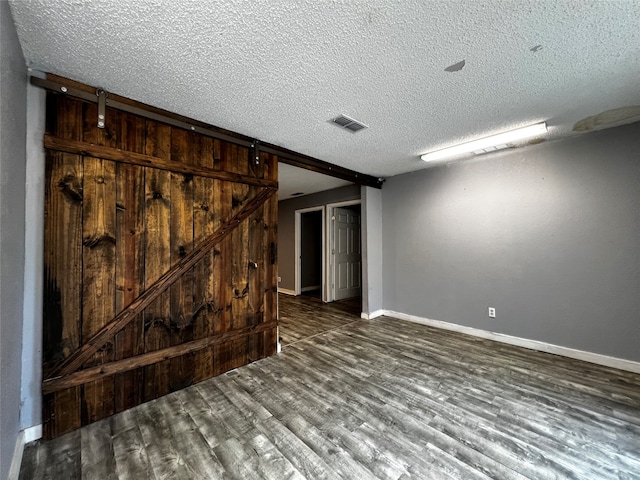 spare room featuring dark hardwood / wood-style floors, a barn door, and a textured ceiling