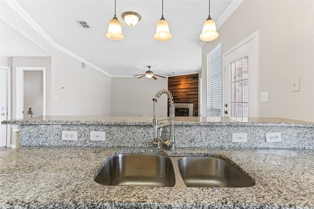 kitchen with hanging light fixtures, sink, crown molding, light stone counters, and ceiling fan