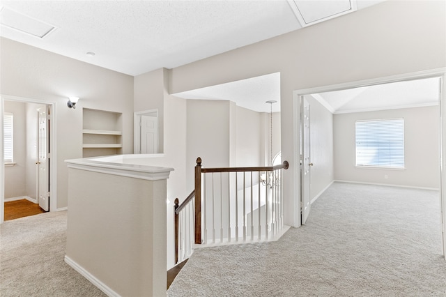 hall featuring built in shelves, a textured ceiling, and light colored carpet